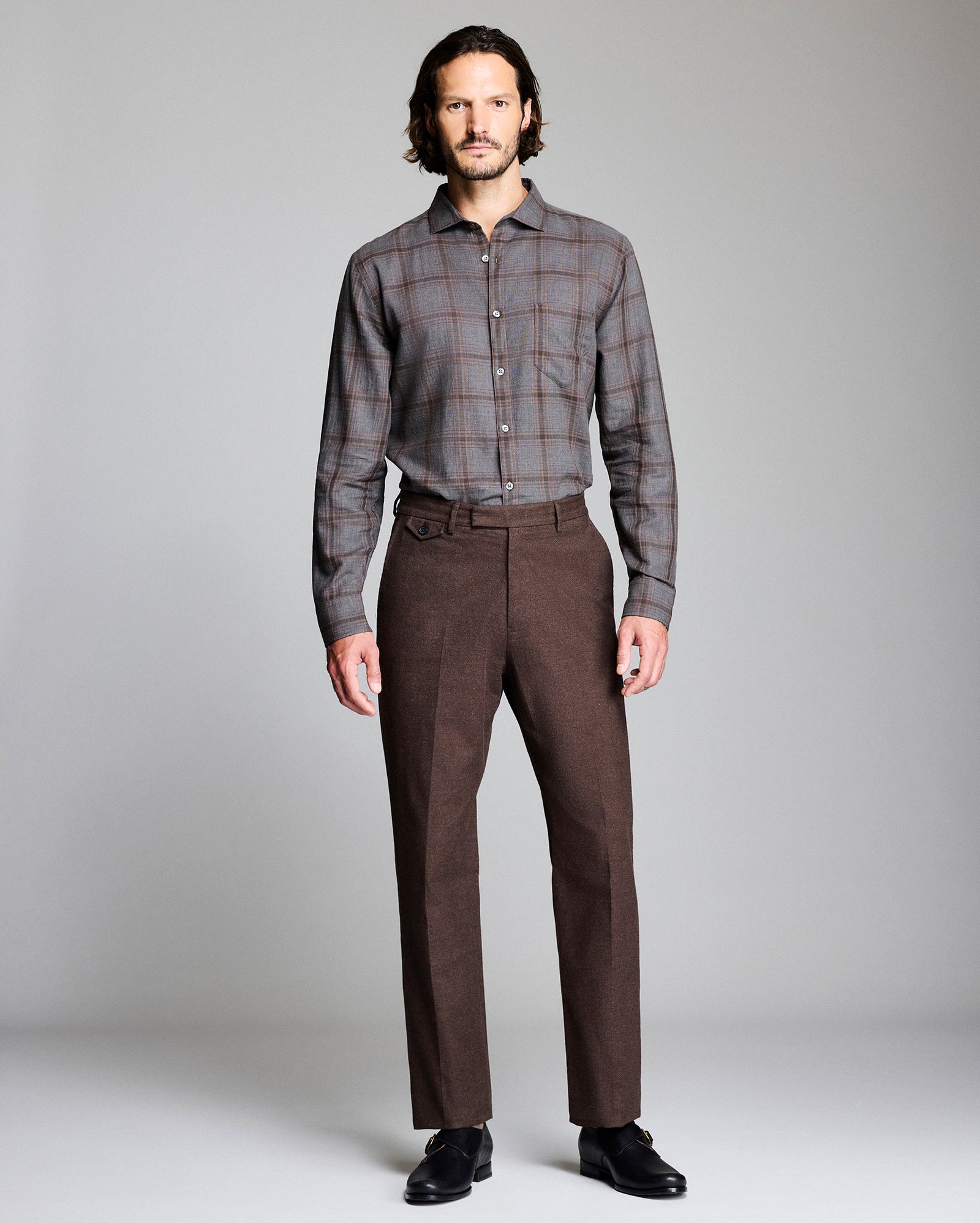 Man wearing a plaid shirt and brown trousers on a plain background