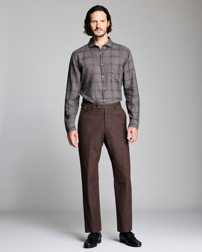 Man wearing a plaid shirt and brown trousers on a plain background