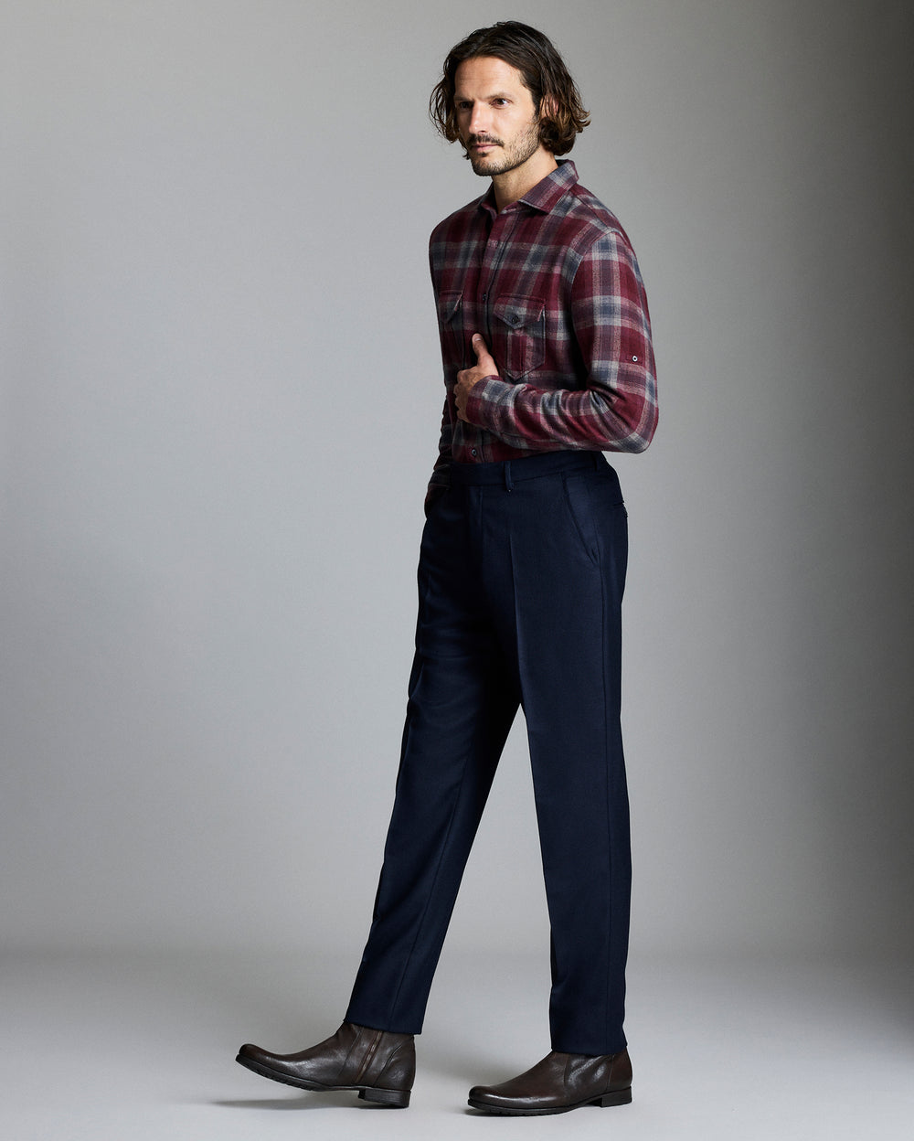 Man wearing a plaid shirt and dark pants against a gray background