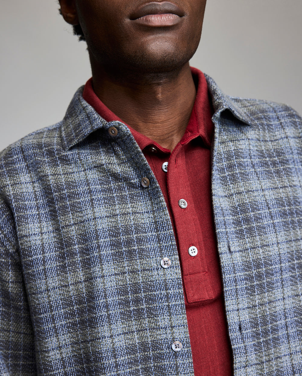 Man wearing a red shirt and blue checkered jacket against a neutral background