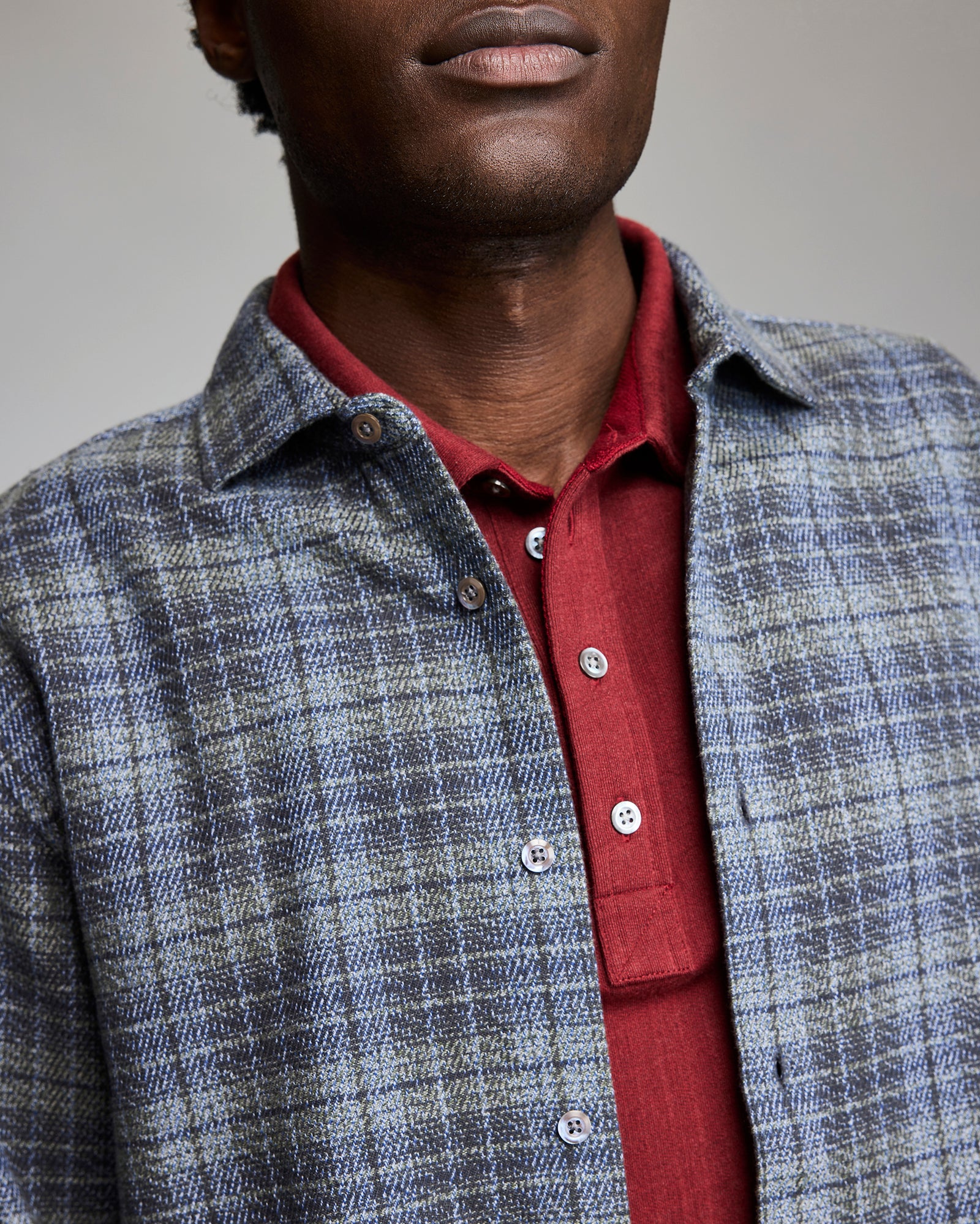 Man wearing a red shirt and blue checkered jacket against a neutral background