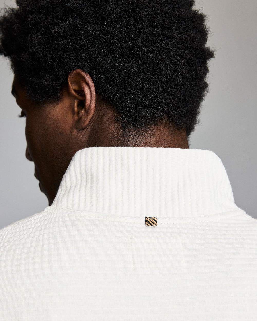 Person wearing a white sweater with a brand logo on a gray background