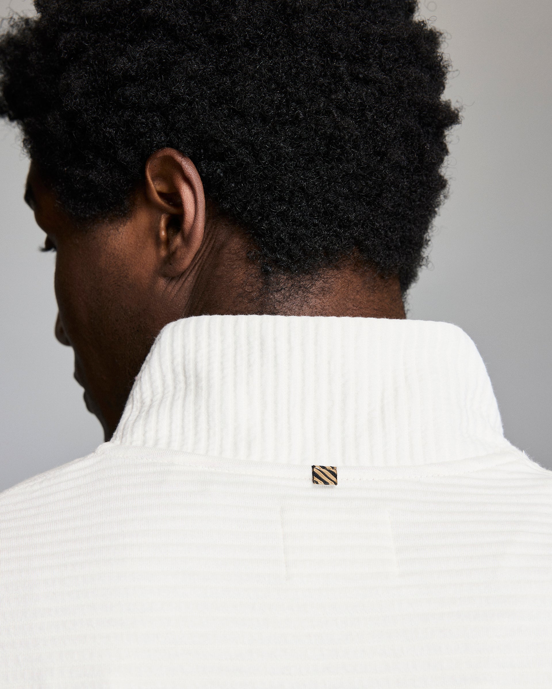 Person wearing a white sweater with a brand logo on a gray background