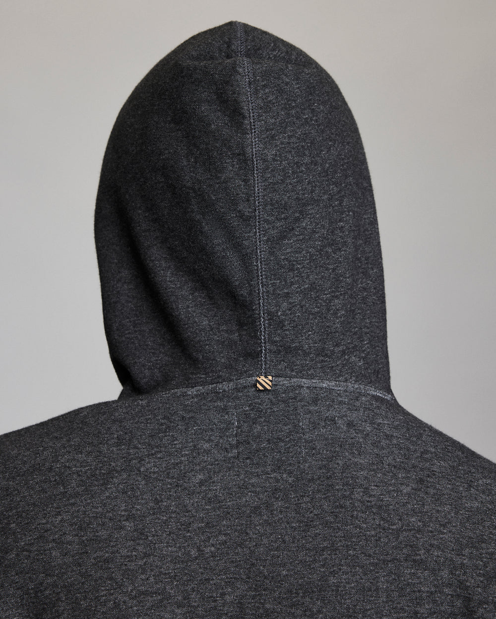 A close-up of the back of a dark gray hooded sweatshirt, showing the hood up and a small stitched tag detail at the center seam near the neckline.