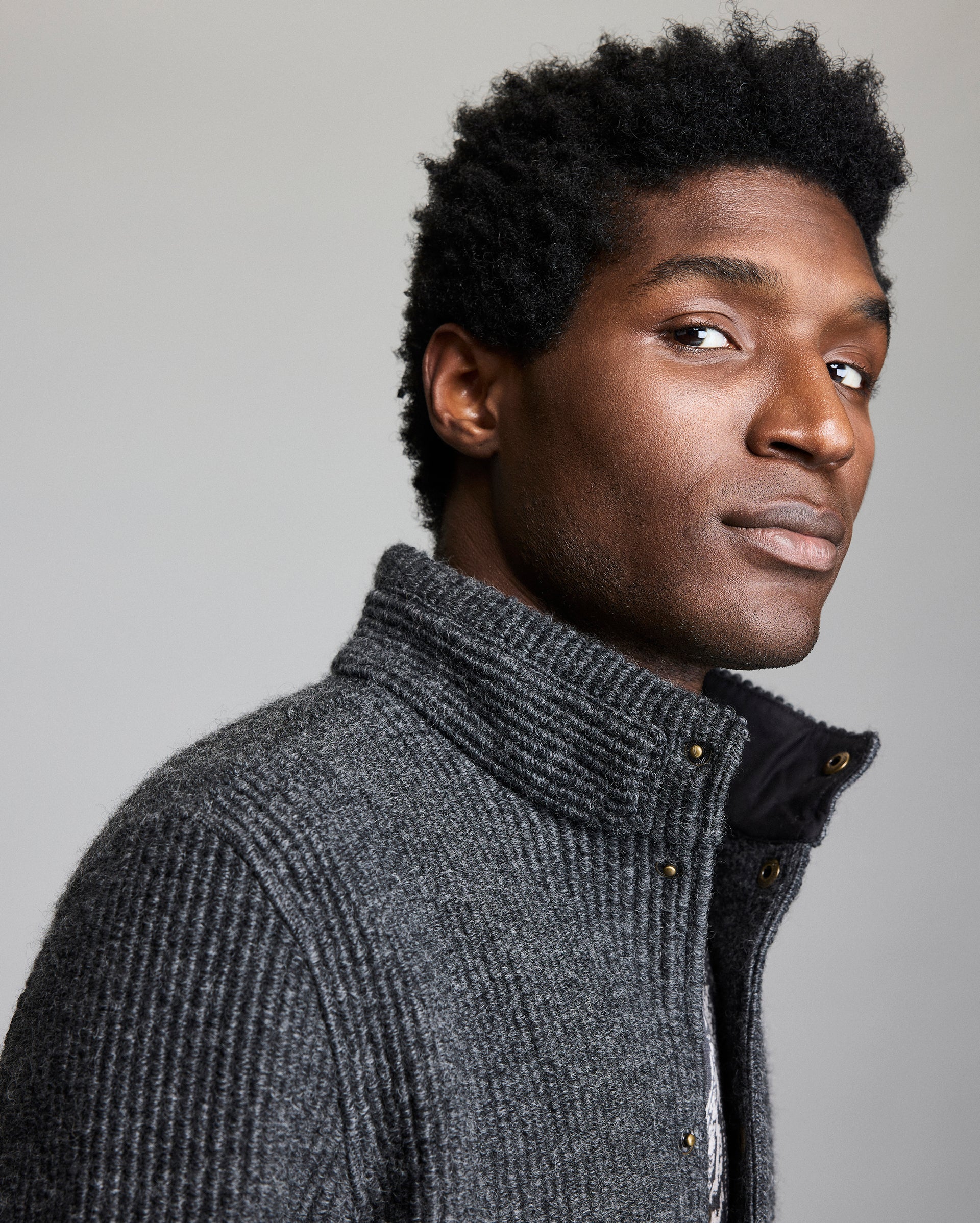 Man wearing a gray knitted jacket against a plain background