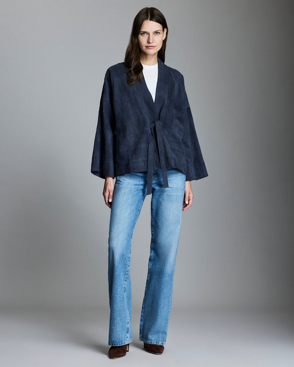 Woman wearing a navy jacket and blue jeans against a gray background