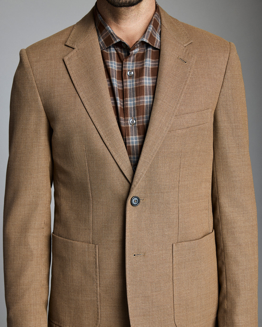 Brown blazer over a plaid shirt on a gray background
