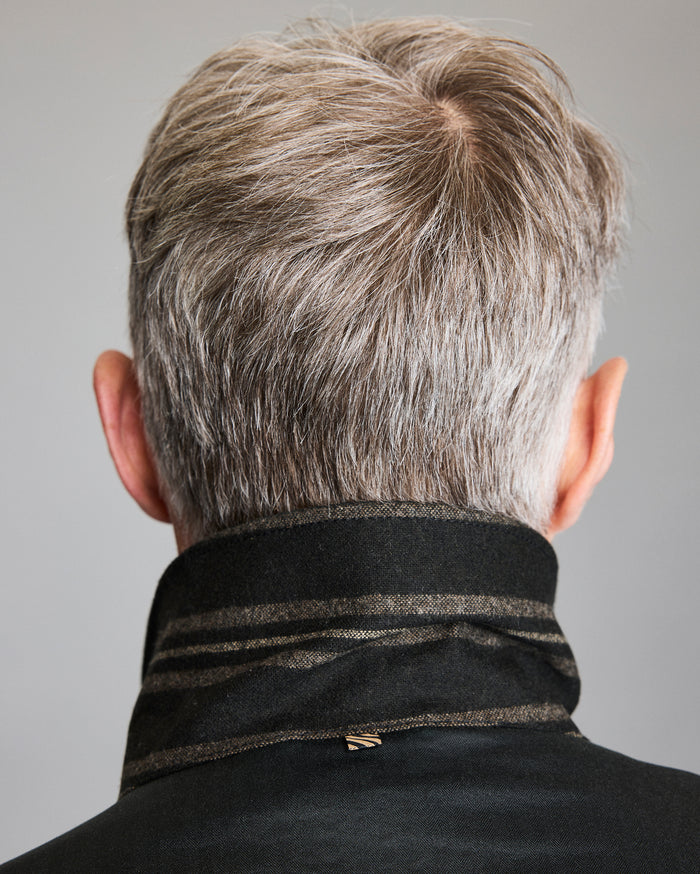 A person with short, gray hair is shown from behind, wearing a dark coat with the collar turned up. The background is plain and neutral.