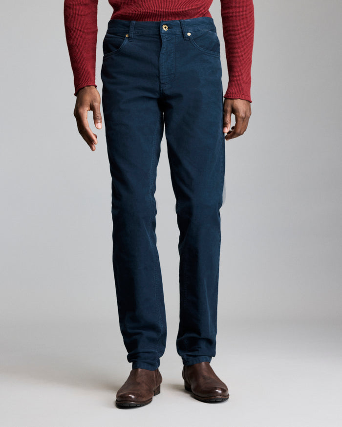 A person wearing a red long-sleeve shirt, dark blue pants, and brown shoes stands against a plain gray background, shown from shoulders to feet.