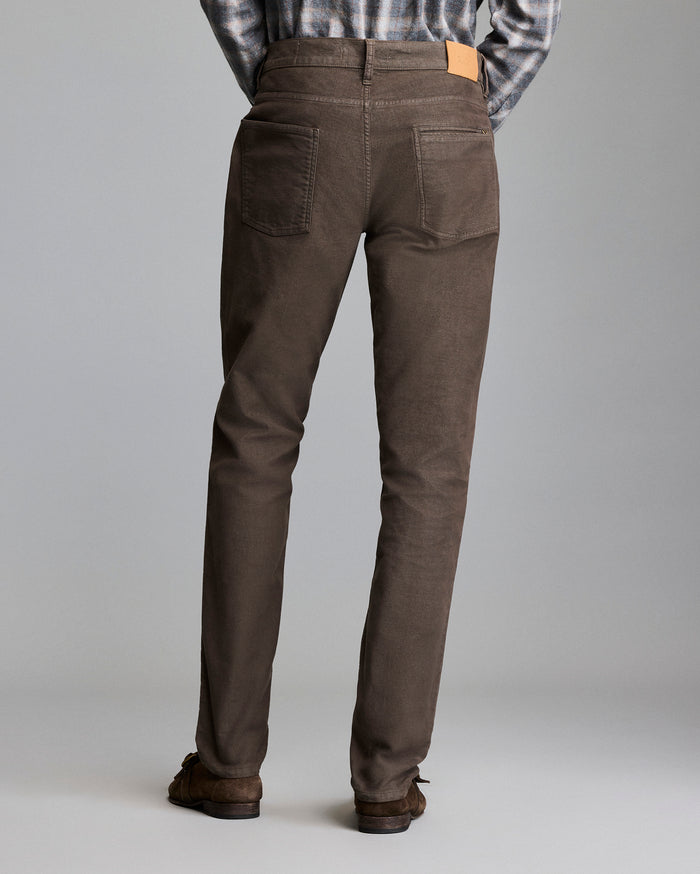 A person wearing brown pants, brown shoes, and a plaid shirt stands facing away from the camera against a plain gray background.