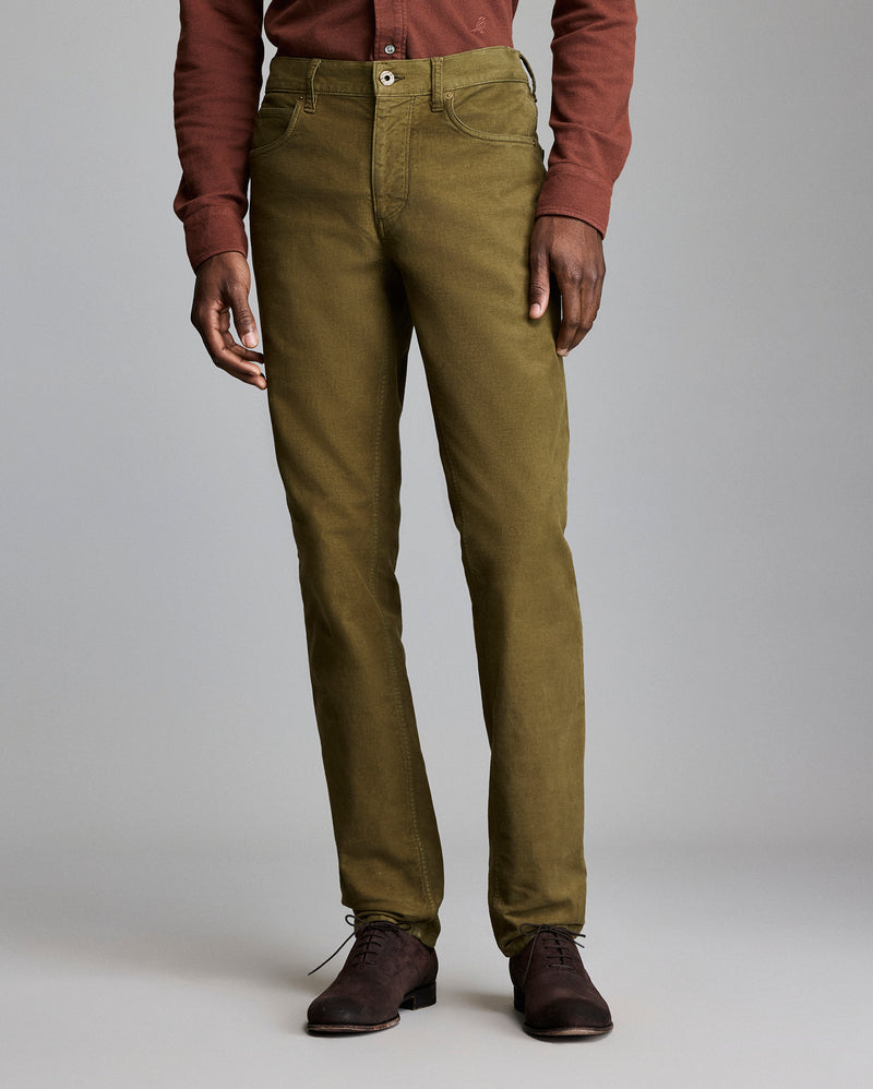 A person wearing olive green straight-leg pants, a rust-colored long-sleeve shirt, and dark brown shoes stands against a plain gray background. Alternate