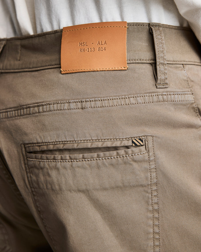 Close-up of the back waistband and pocket of khaki pants. A tan leather patch with the text MSL • ALA RN-113 814 is sewn above the pocket. A white shirt is partially visible above the pants.