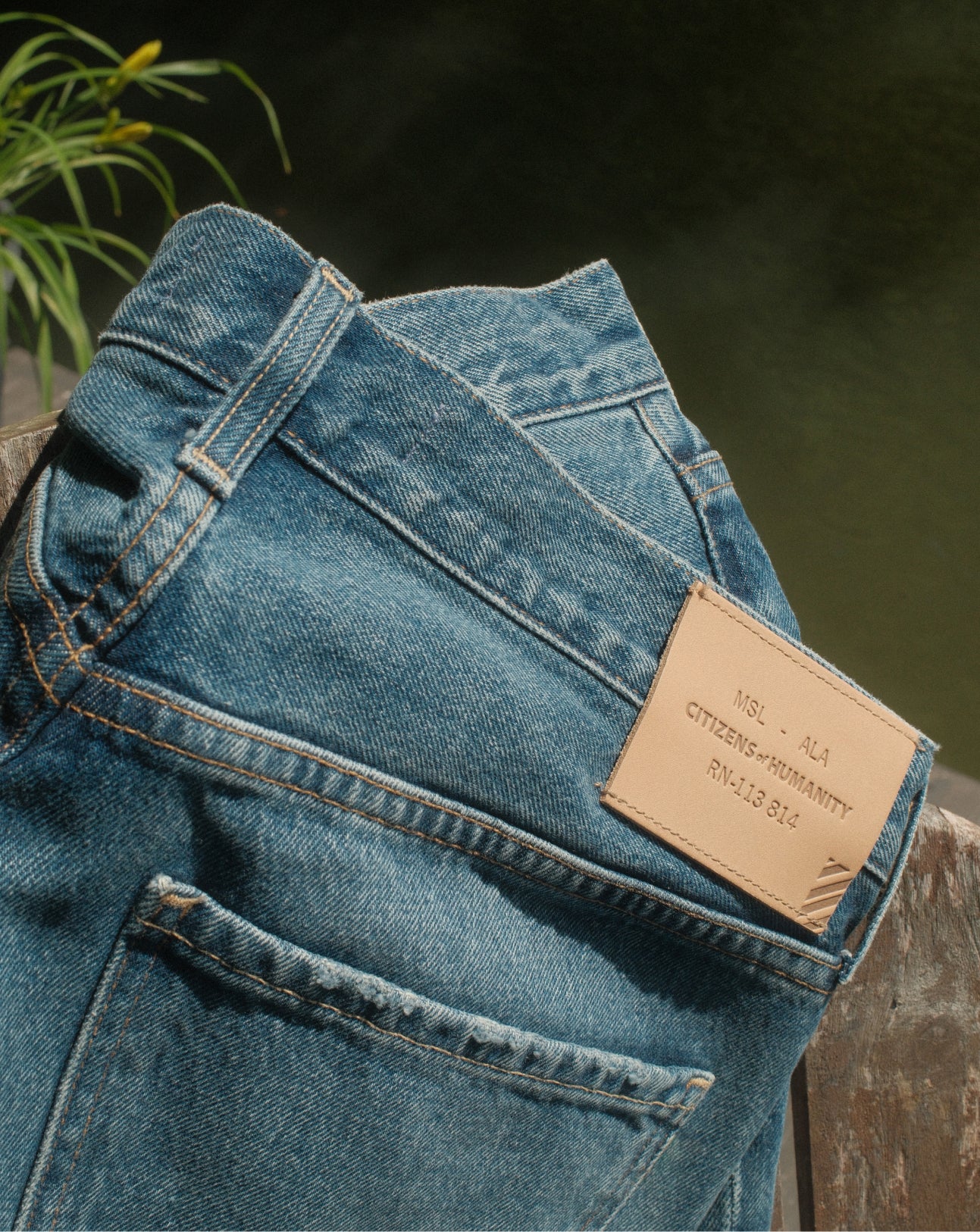 Folded blue denim jeans with a brown leather label on a blurred natural background