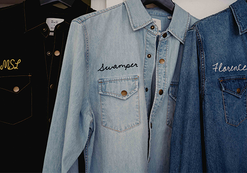 Two denim shirts with embroidered names on a hanger against a white background