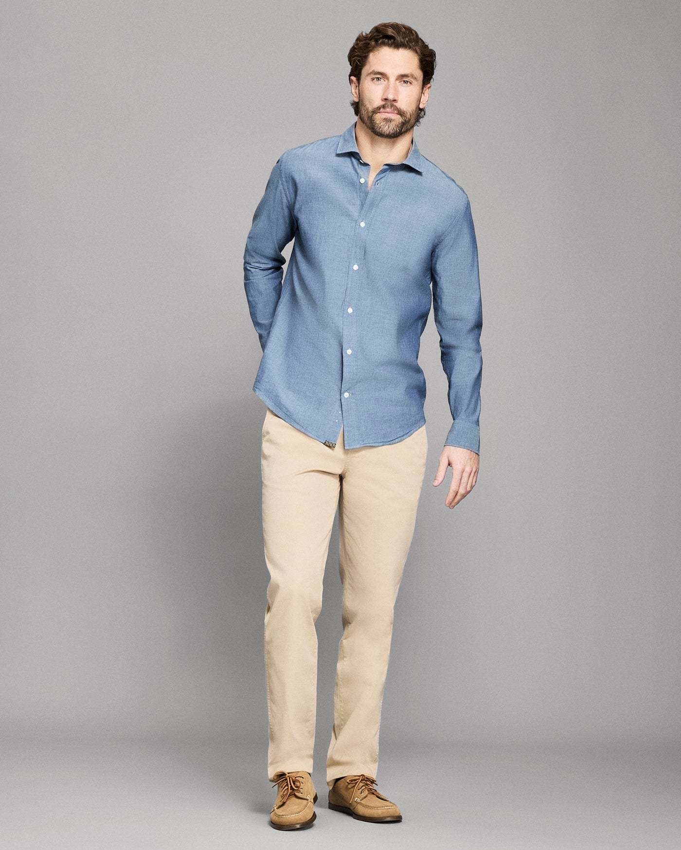 Man wearing a blue shirt and beige pants against a gray background
