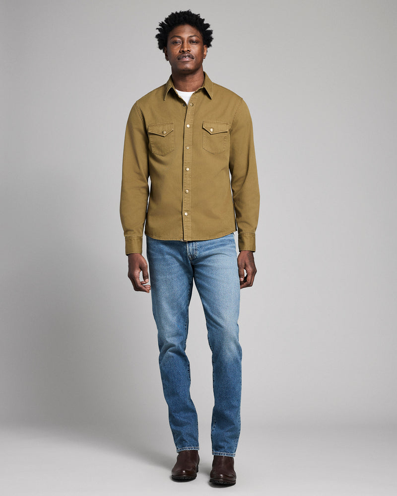 Man wearing a green shirt and blue jeans against a gray background Alternate
