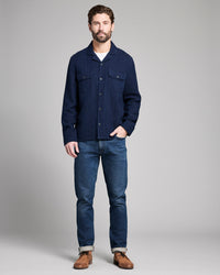 Man wearing a navy blue textured shirt and jeans on a gray background