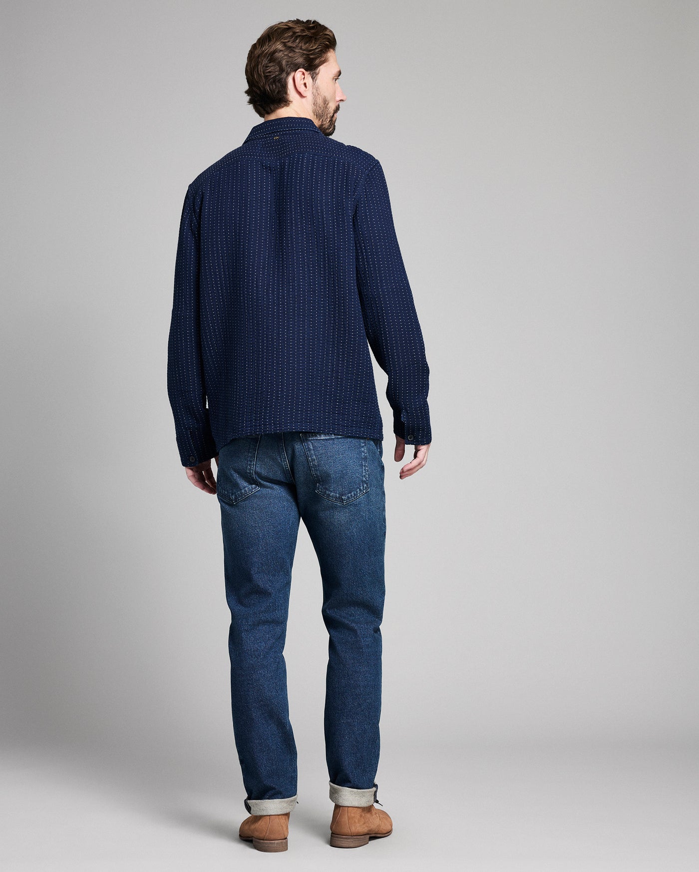 Man wearing a navy sweater and blue jeans on a gray background
