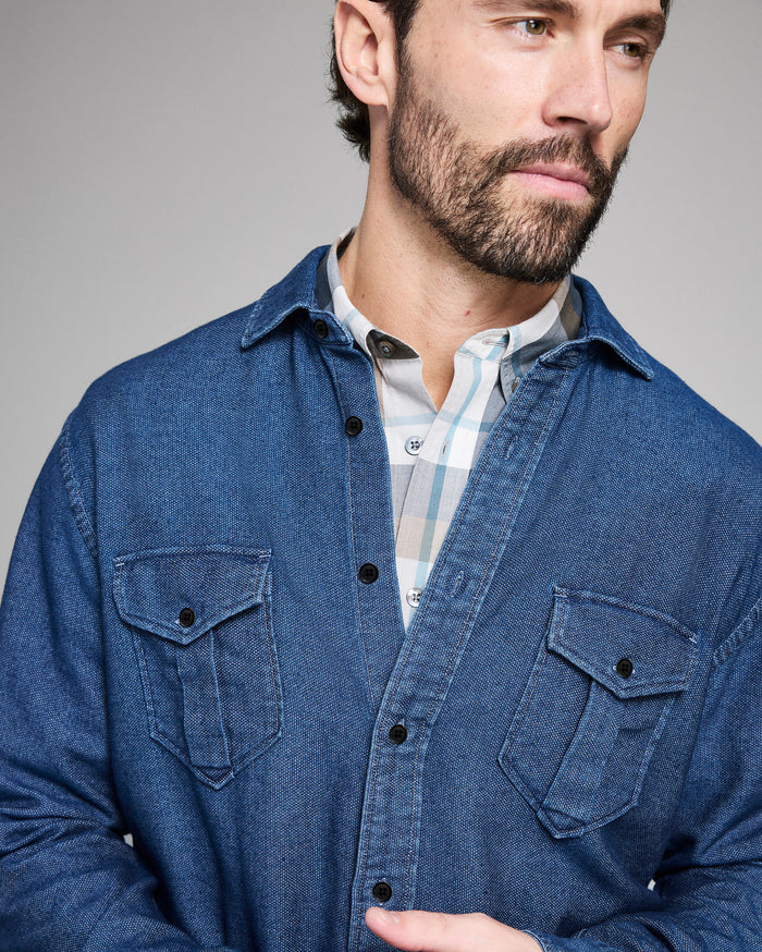 Man wearing a blue denim shirt over a checkered shirt against a gray background