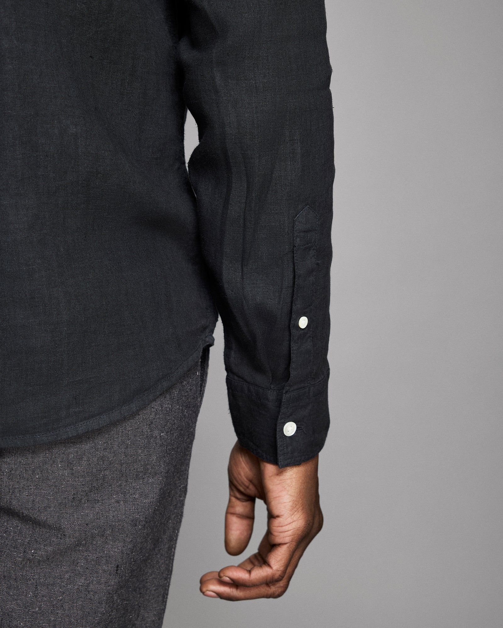 Close-up of a person wearing a black shirt with button details on a gray background