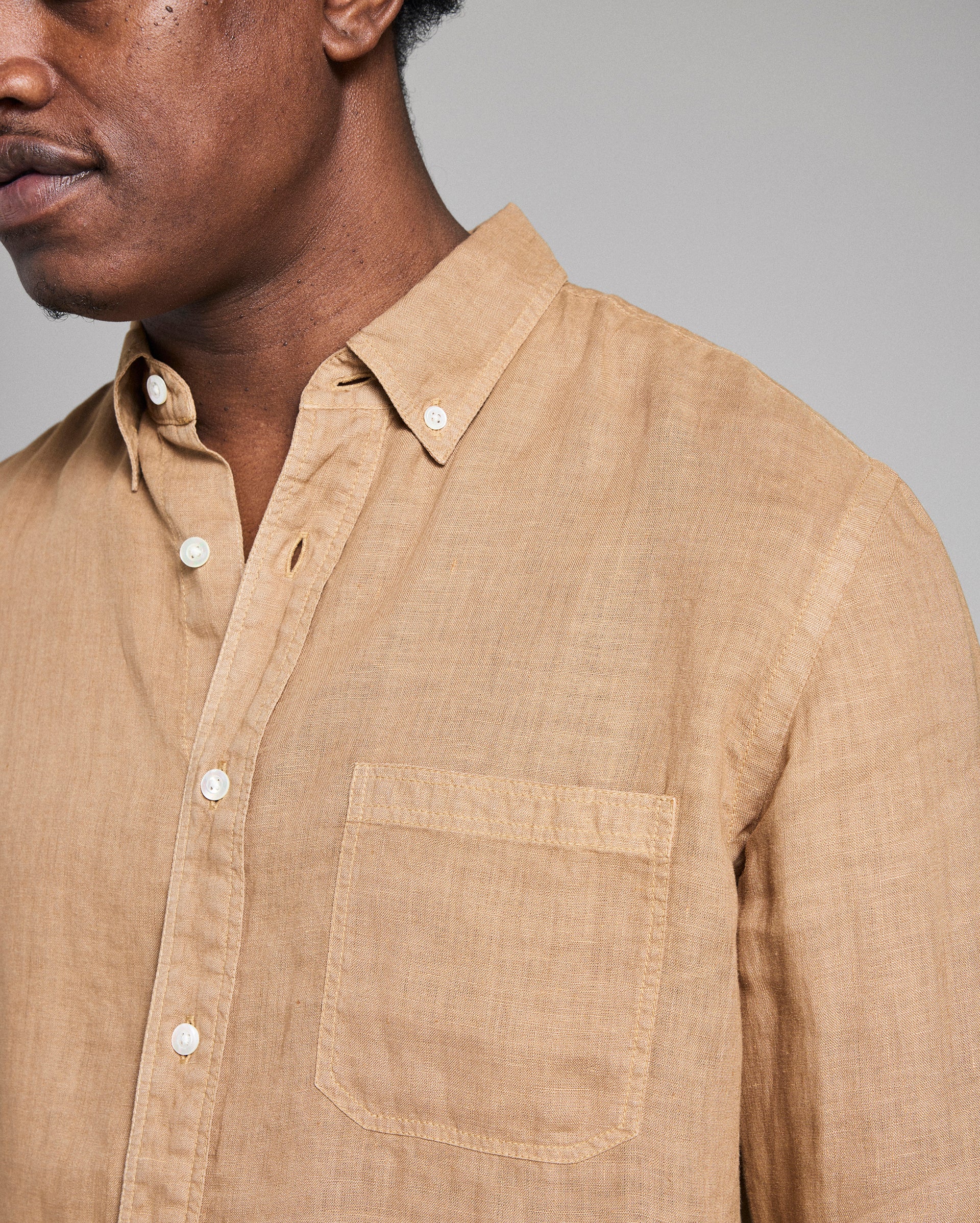 Man wearing a beige button-up shirt against a gray background