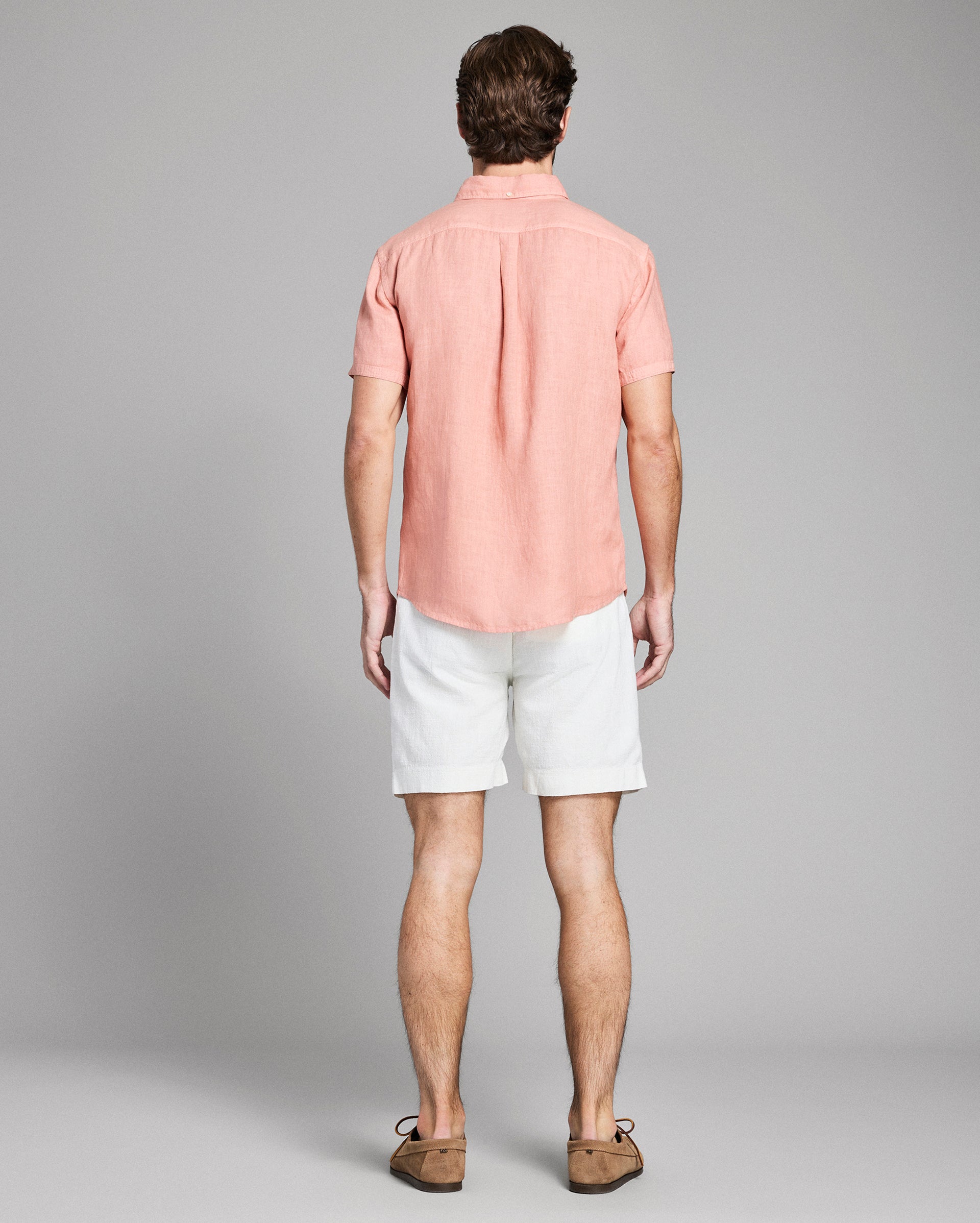 Man wearing a pink shirt and white shorts on a gray background