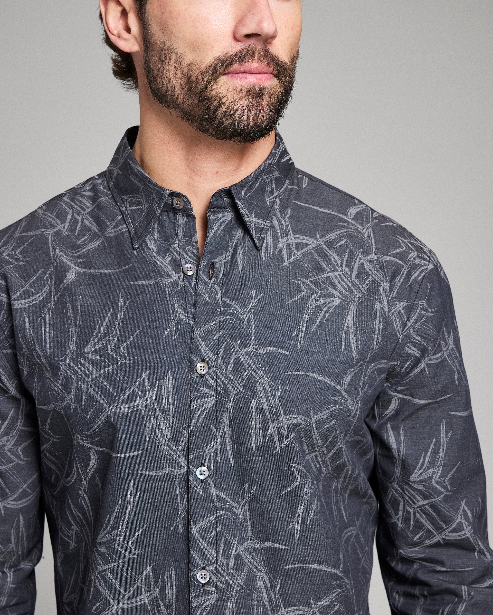 Man wearing a dark gray shirt with a subtle pattern on a plain background