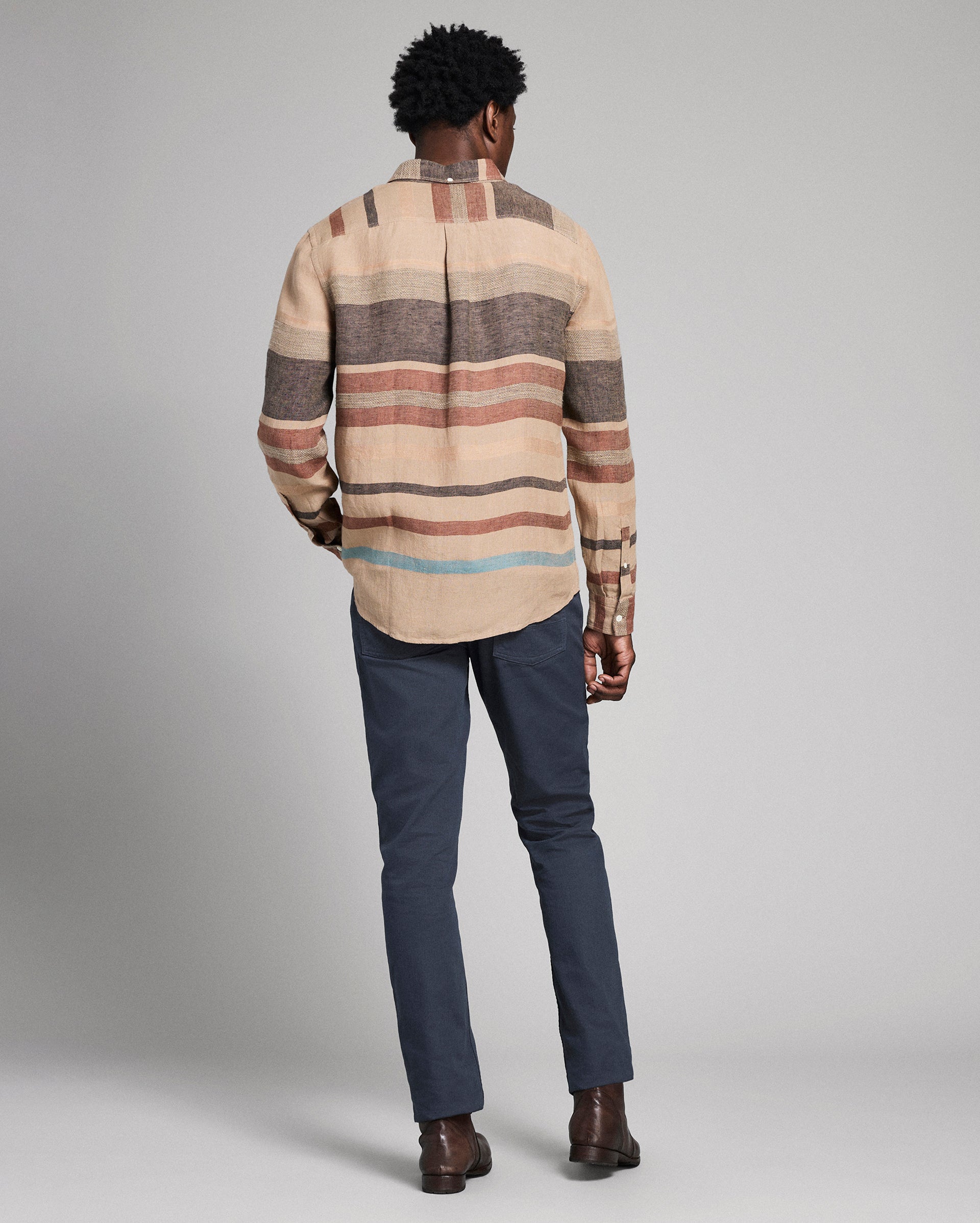 Man wearing a striped shirt and dark pants against a plain background