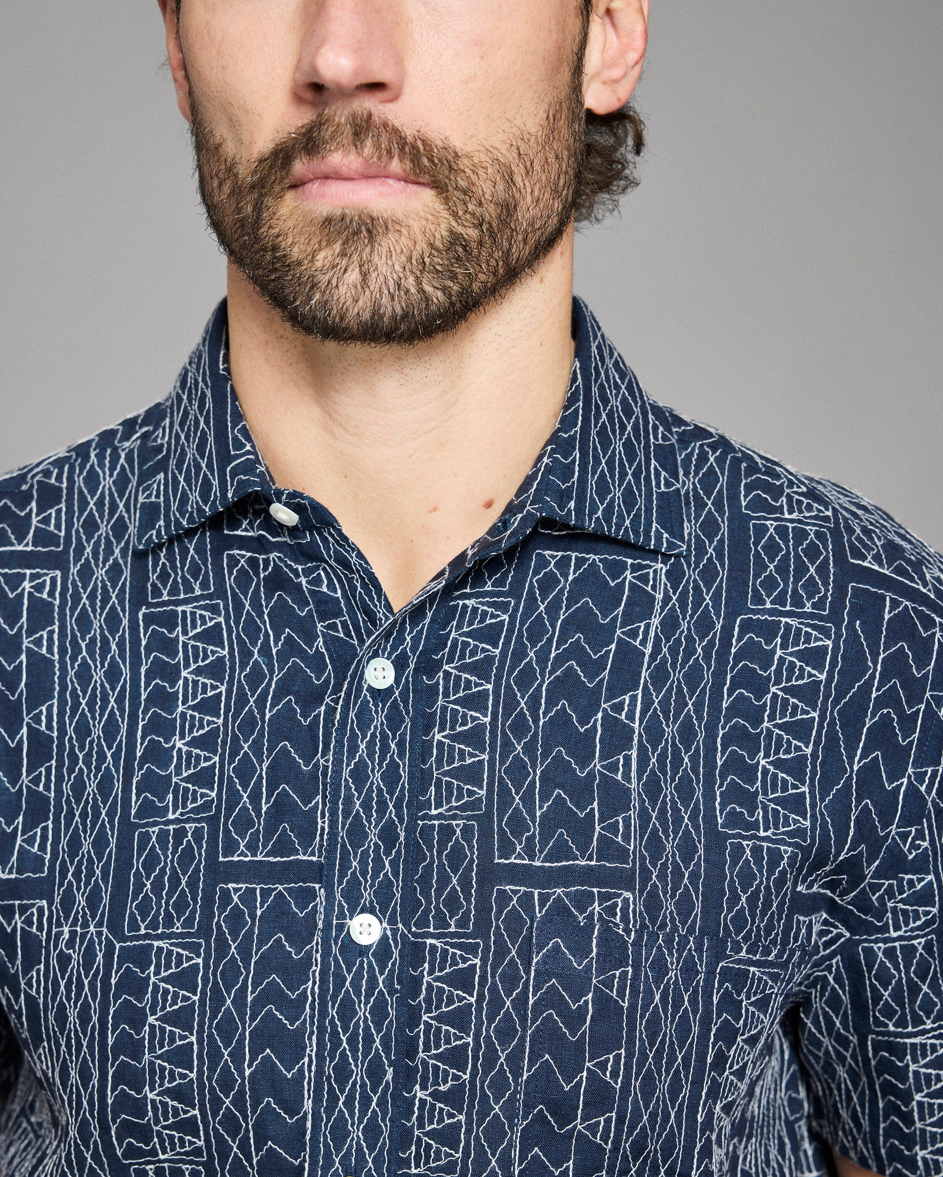 Man wearing a navy blue shirt with white geometric pattern against a gray background
