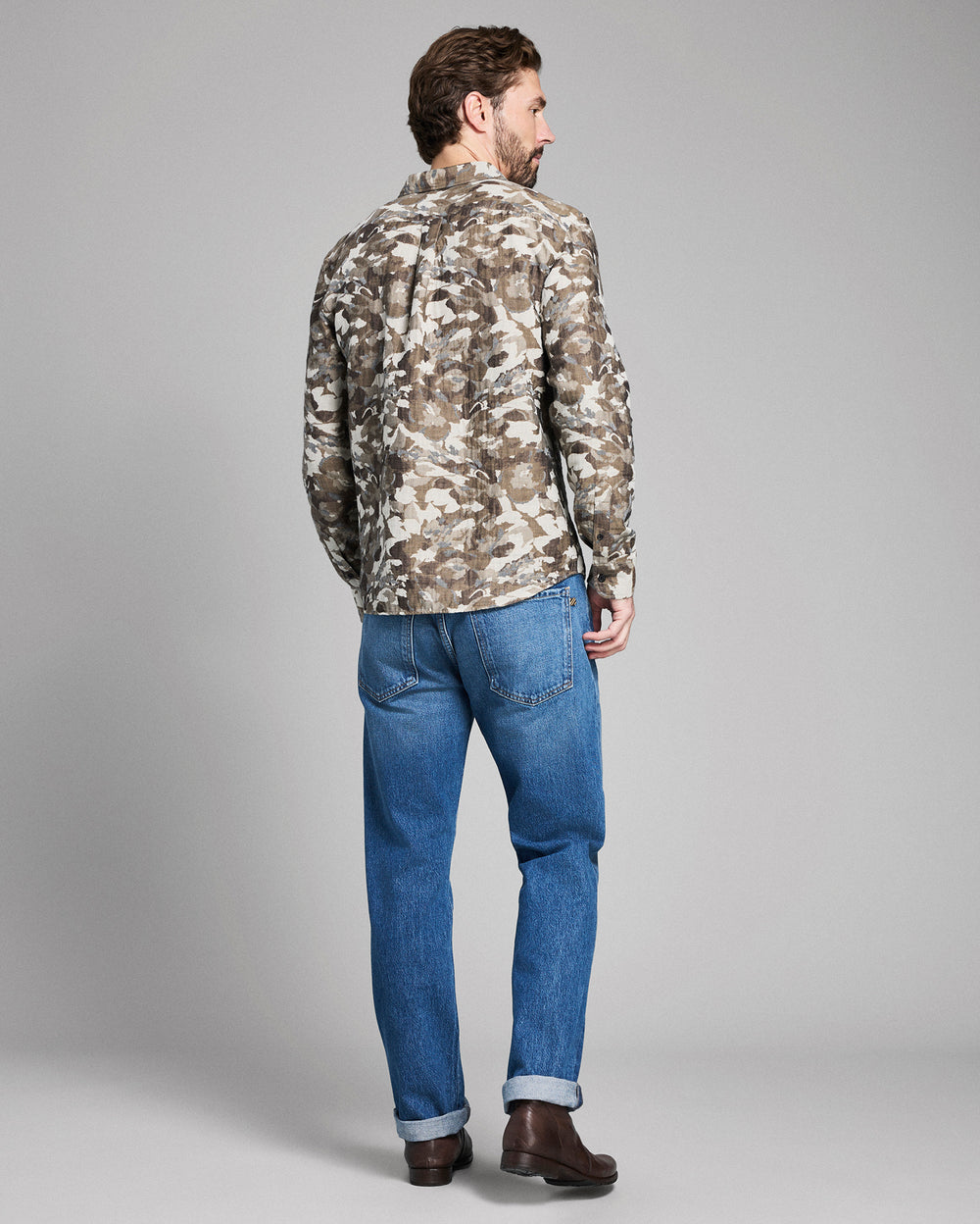 Man wearing a camouflage jacket and blue jeans on a gray background