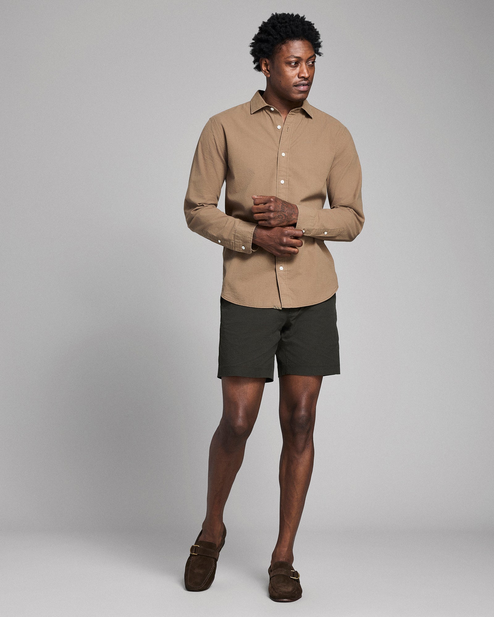 Man wearing a beige shirt and dark shorts on a gray background