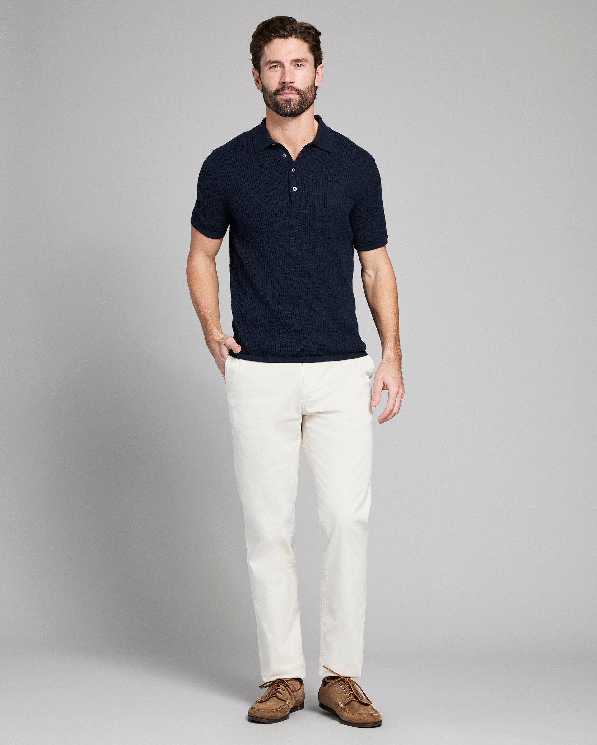 Man wearing a navy polo shirt and white pants on a gray background
