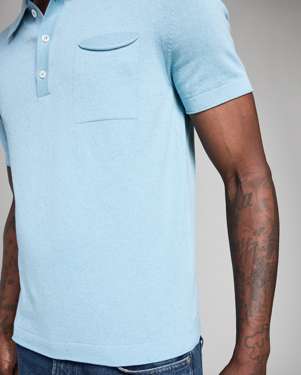 Light blue polo shirt worn by a person with tattoos on arms against a neutral background