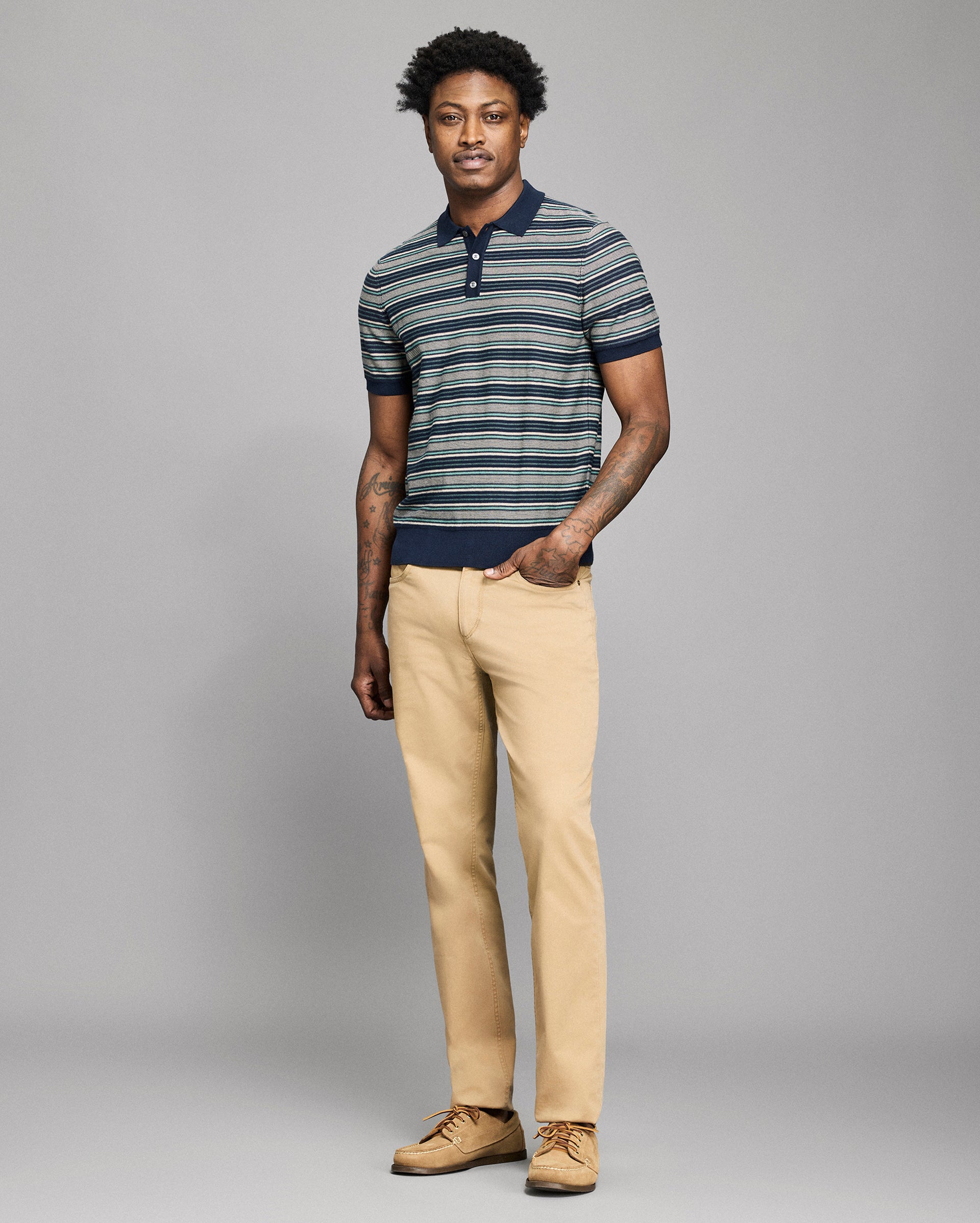 Man wearing a striped polo shirt and beige pants against a gray background