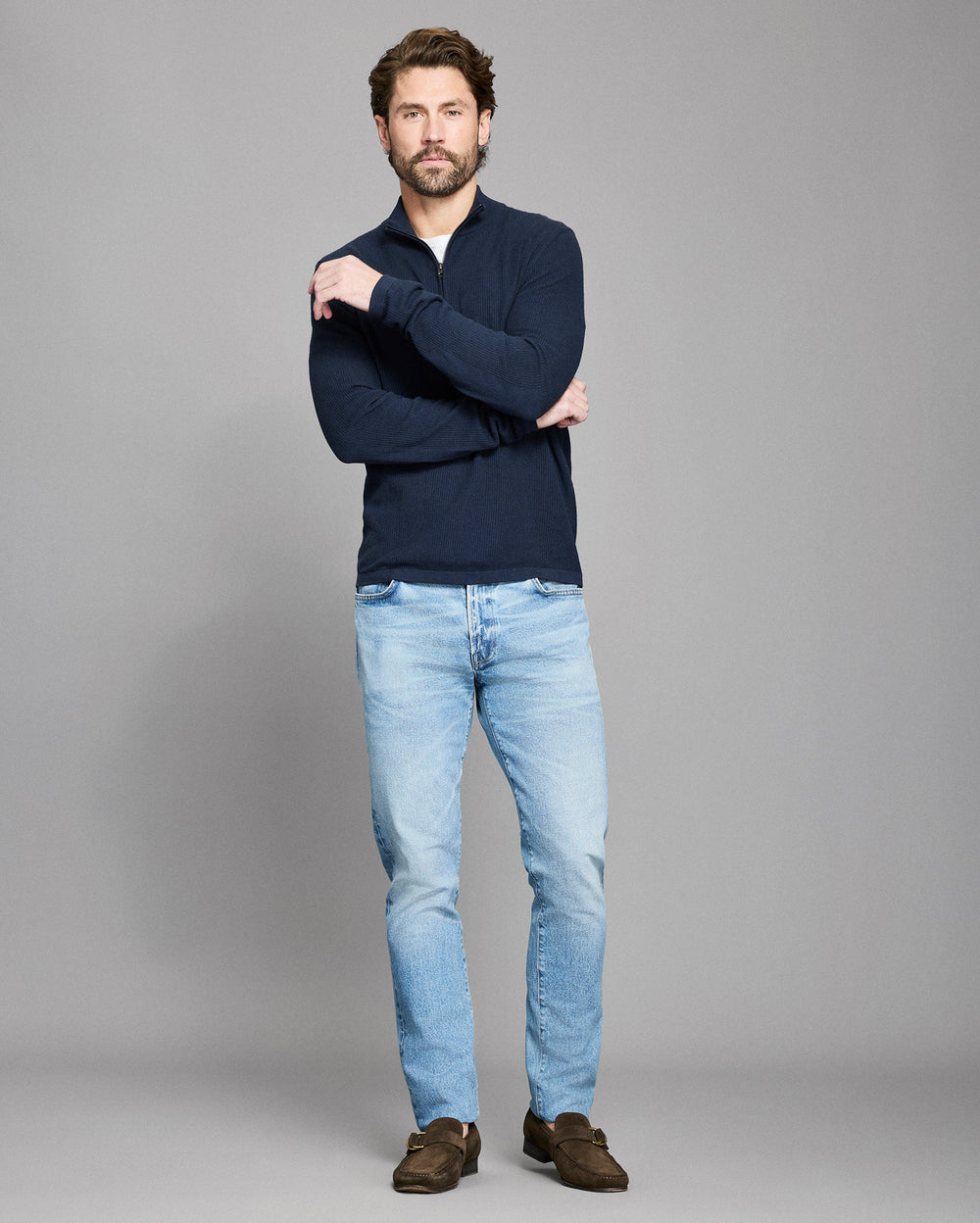Man wearing a navy sweater and light blue jeans on a gray background
