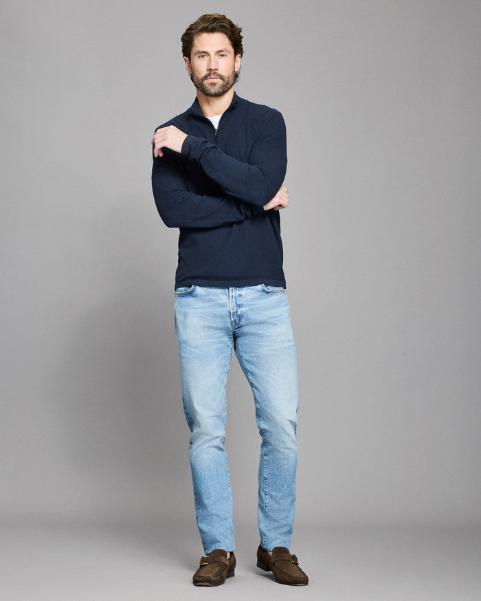 Man wearing a navy sweater and light blue jeans on a gray background