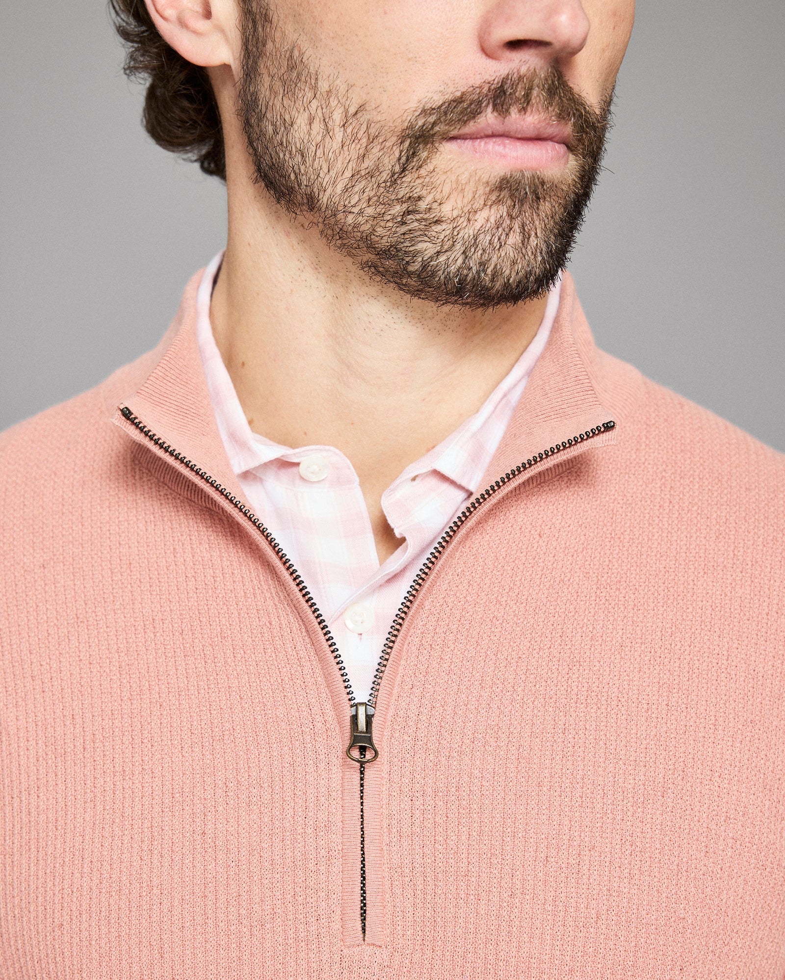 Close-up of a man wearing a pink sweater with a zipper, against a gray background