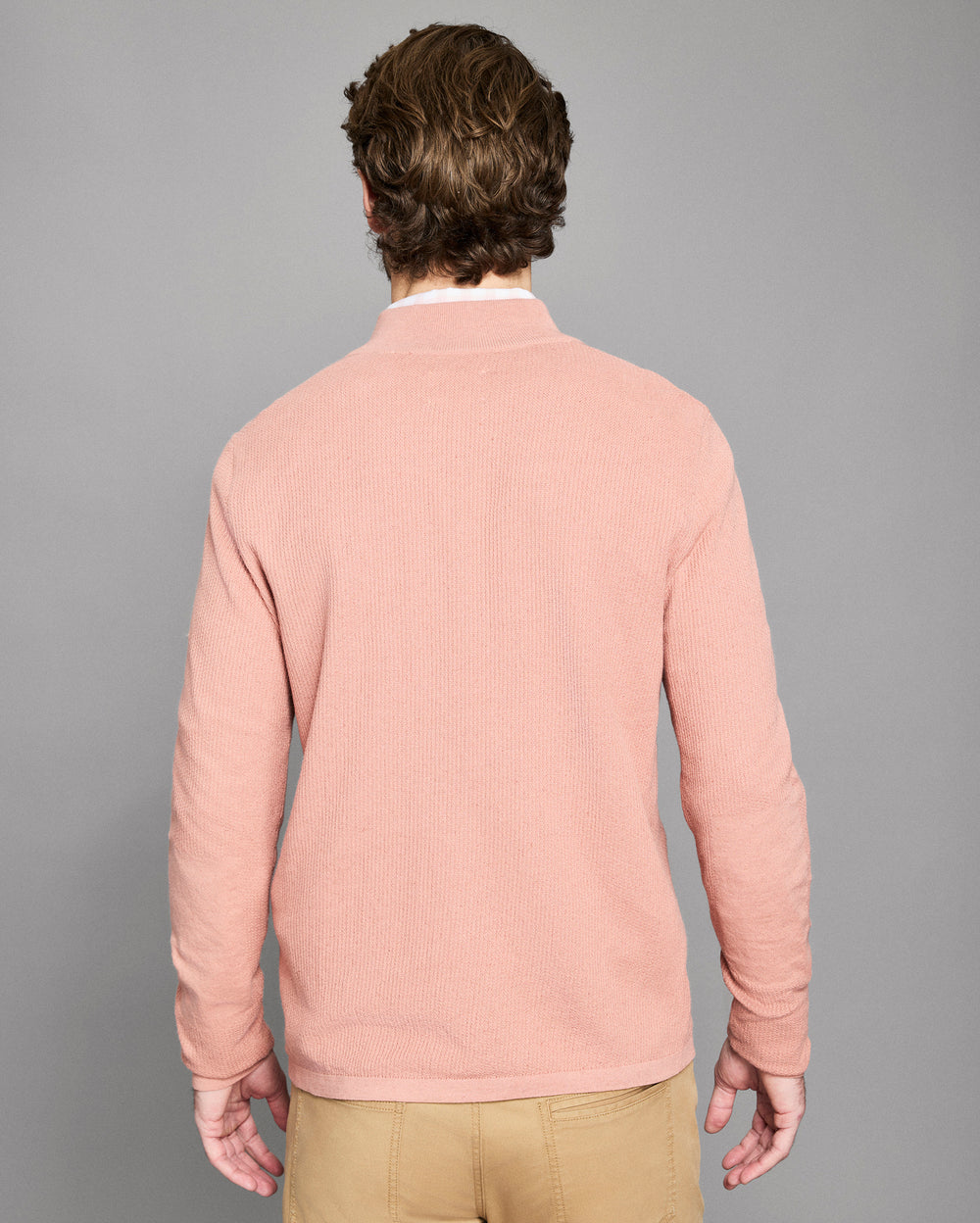 Man wearing a pink sweater against a gray background