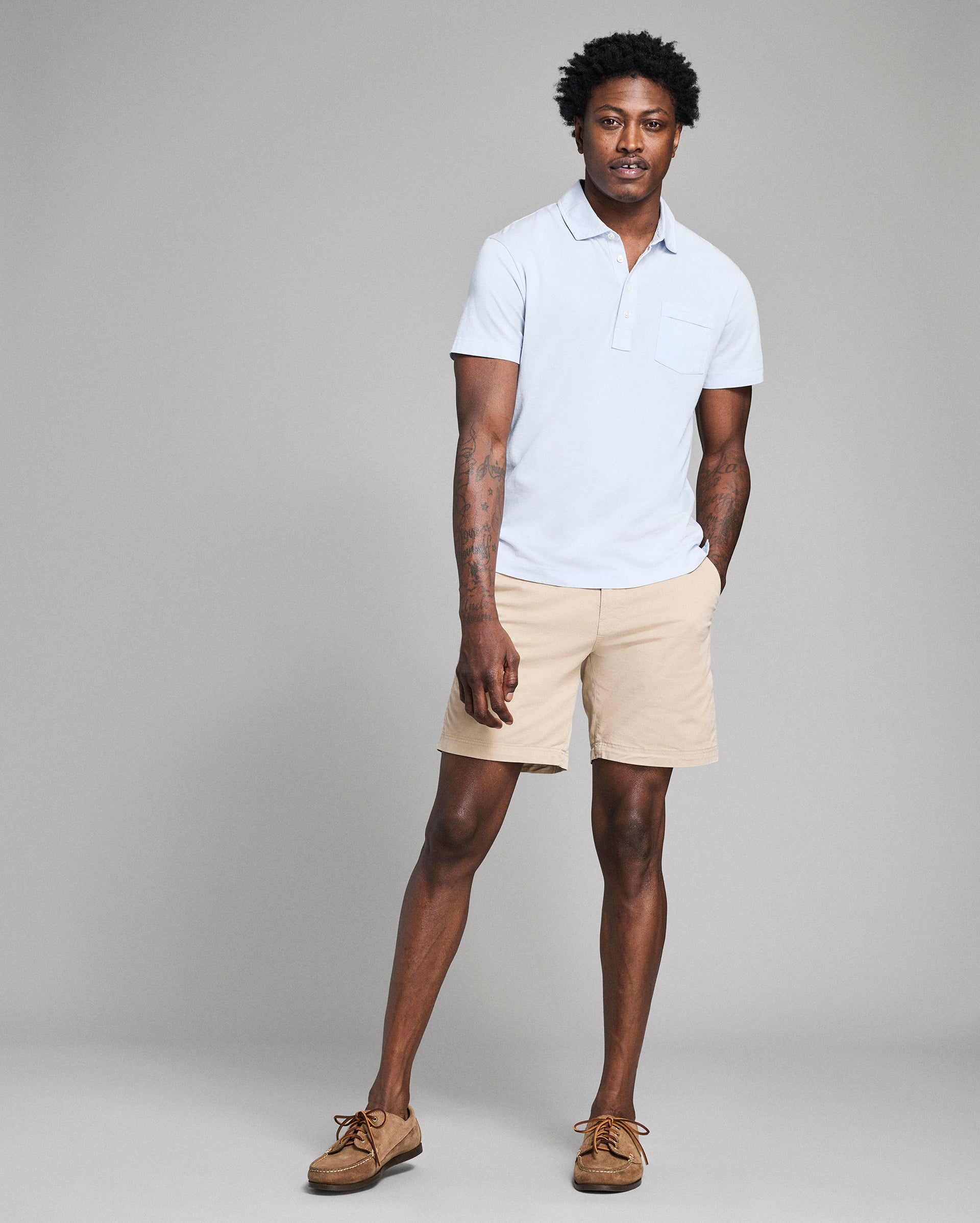 Man wearing a white polo shirt and beige shorts against a gray background