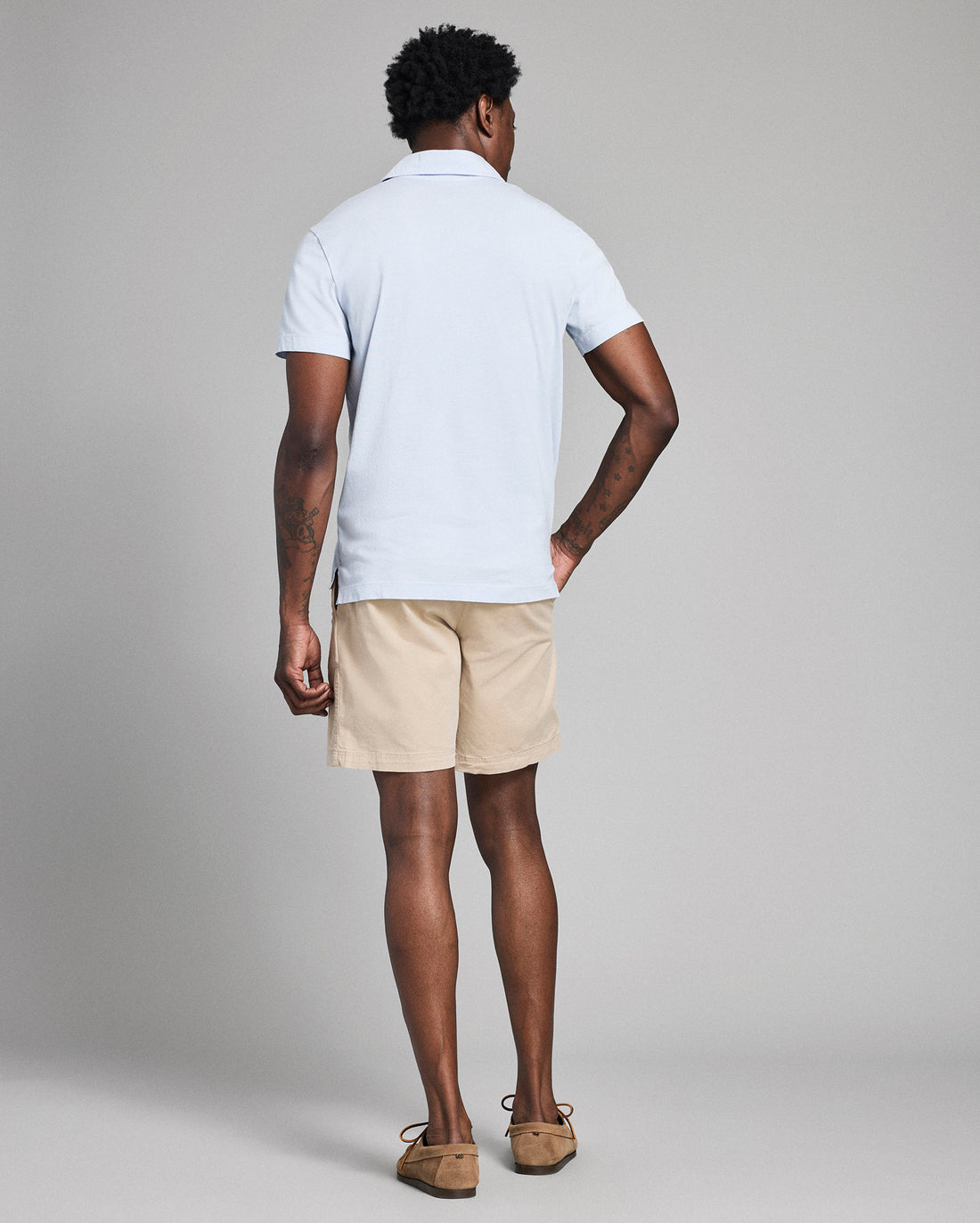 Man wearing a white polo shirt and beige shorts on a gray background
