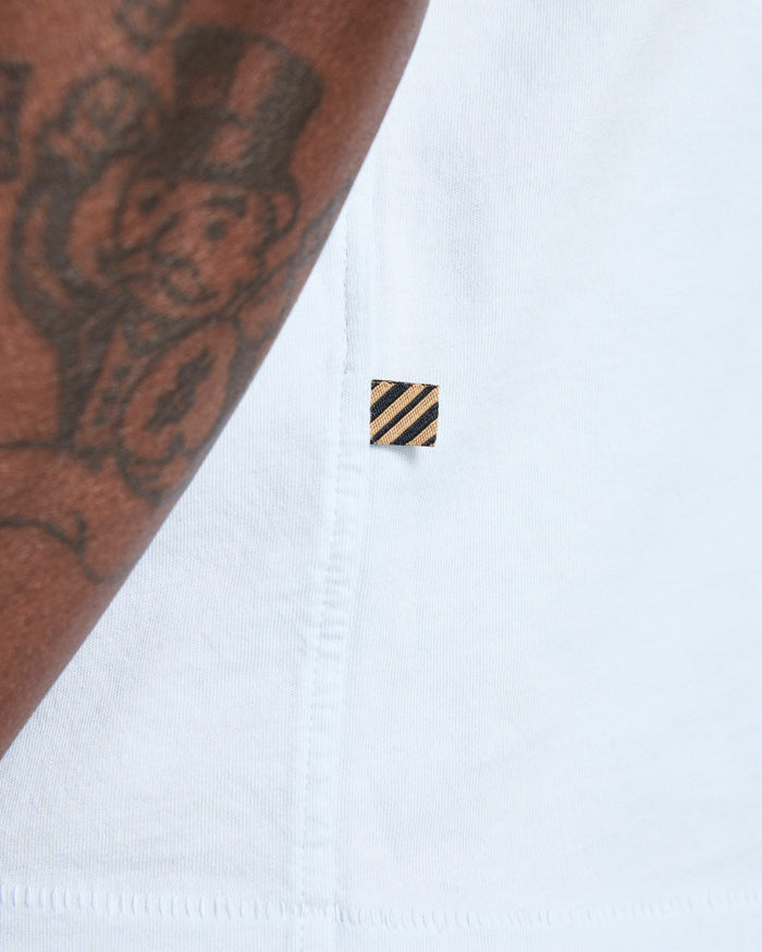 Close-up of a white shirt with a small black and gold logo on a white background