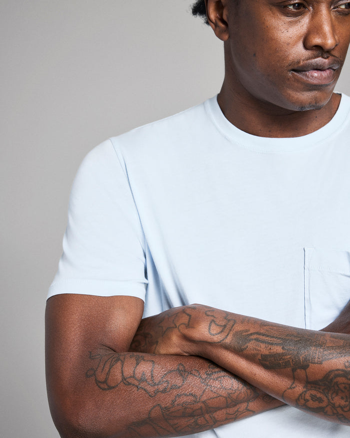 Man wearing a white t-shirt with tattoos on his arms against a plain background