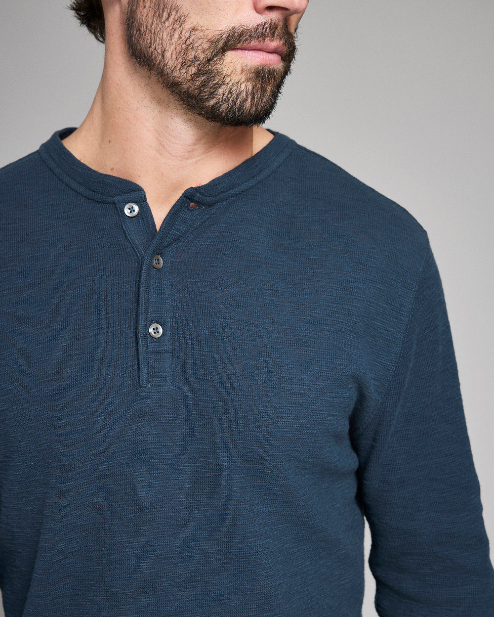 Man wearing a blue henley shirt against a gray background