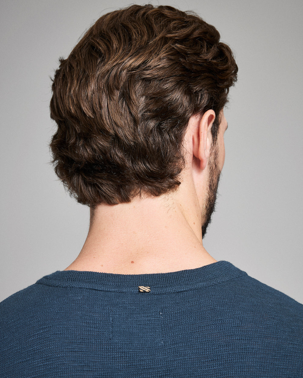 Man with styled hair from behind wearing a blue shirt on a gray background
