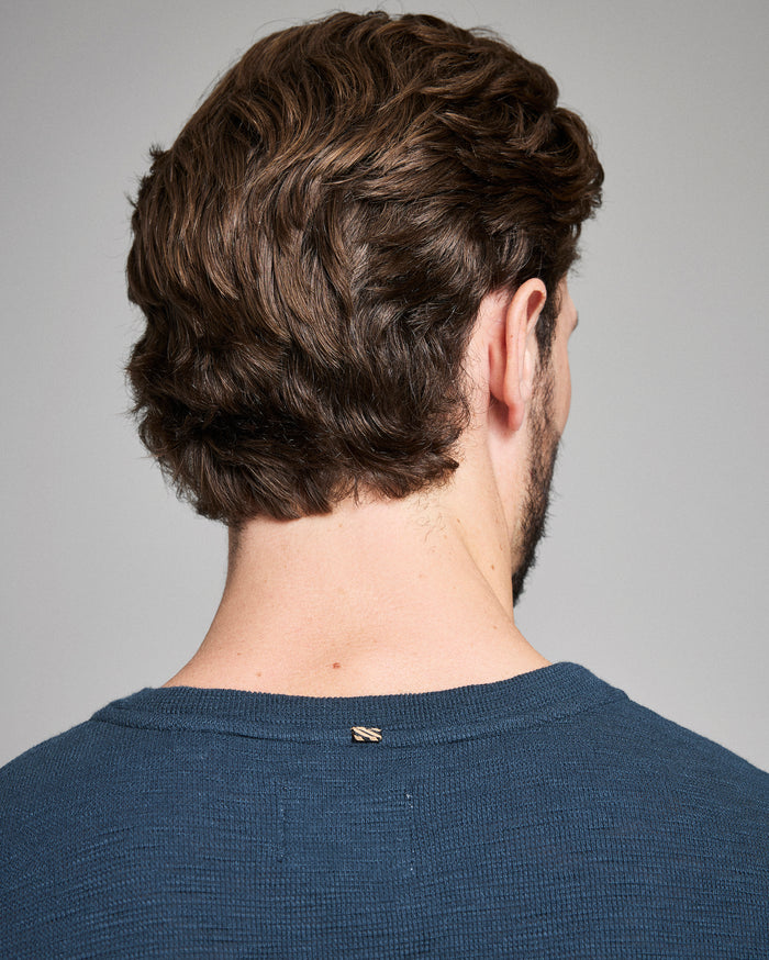 Man with styled hair from behind wearing a blue shirt on a gray background