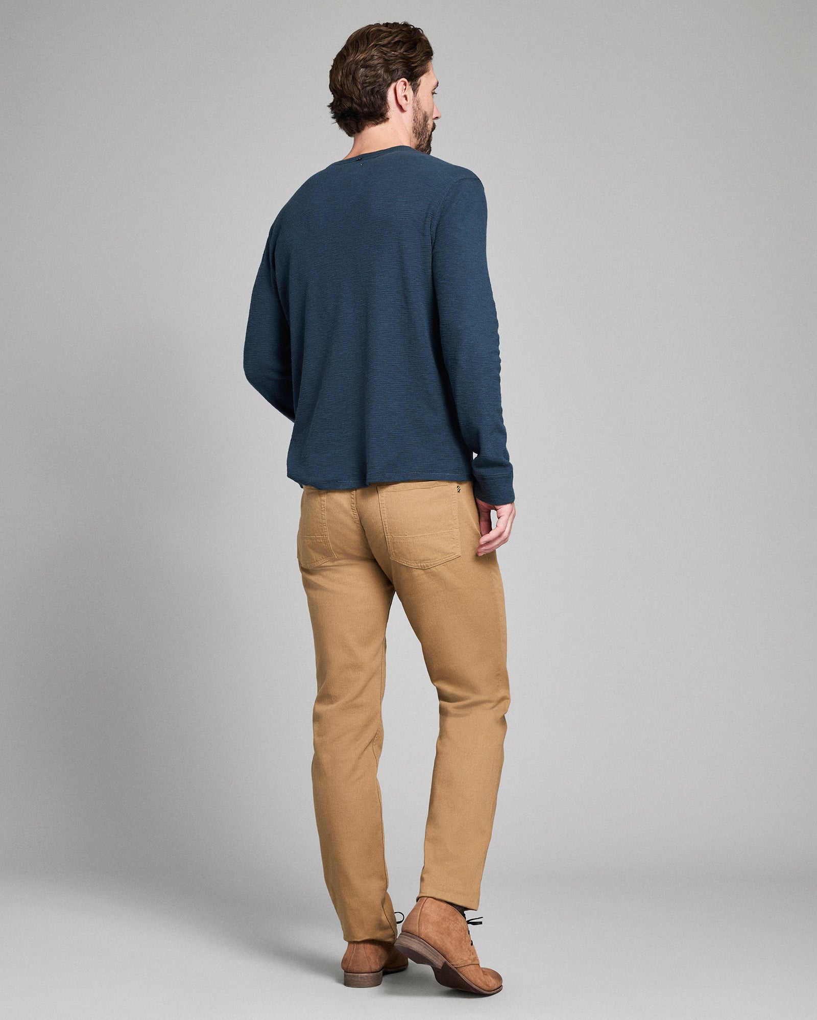 Man wearing a blue sweater and beige pants against a gray background