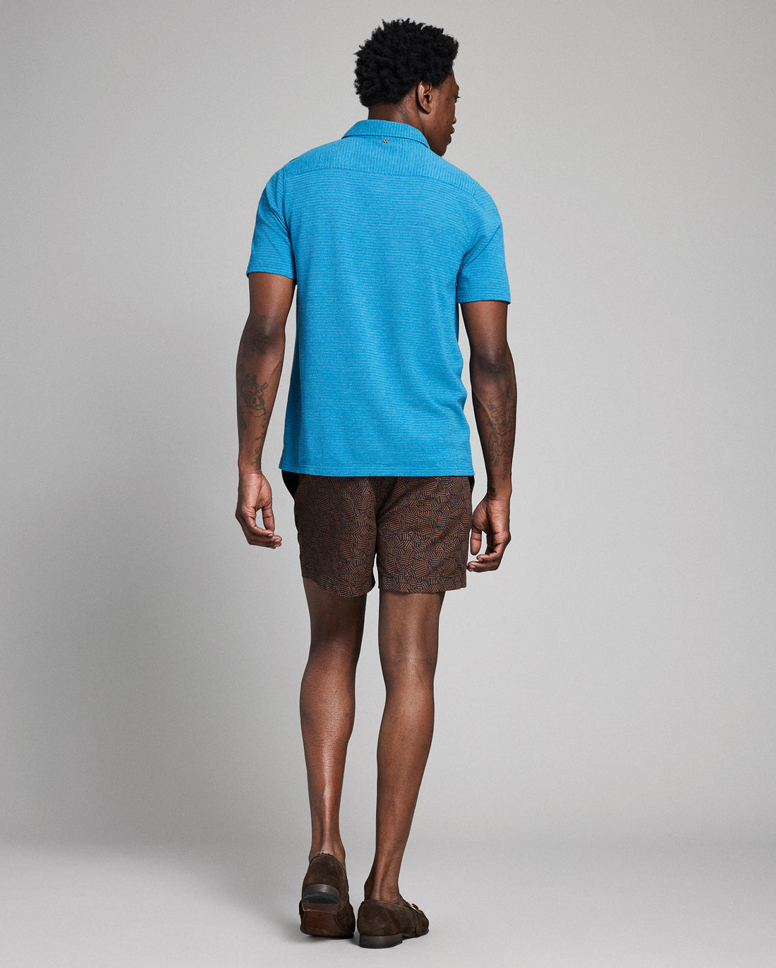 Man wearing a blue polo shirt and patterned shorts on a gray background