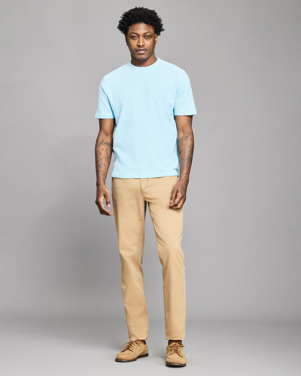 Man wearing a light blue t-shirt and beige pants against a gray background