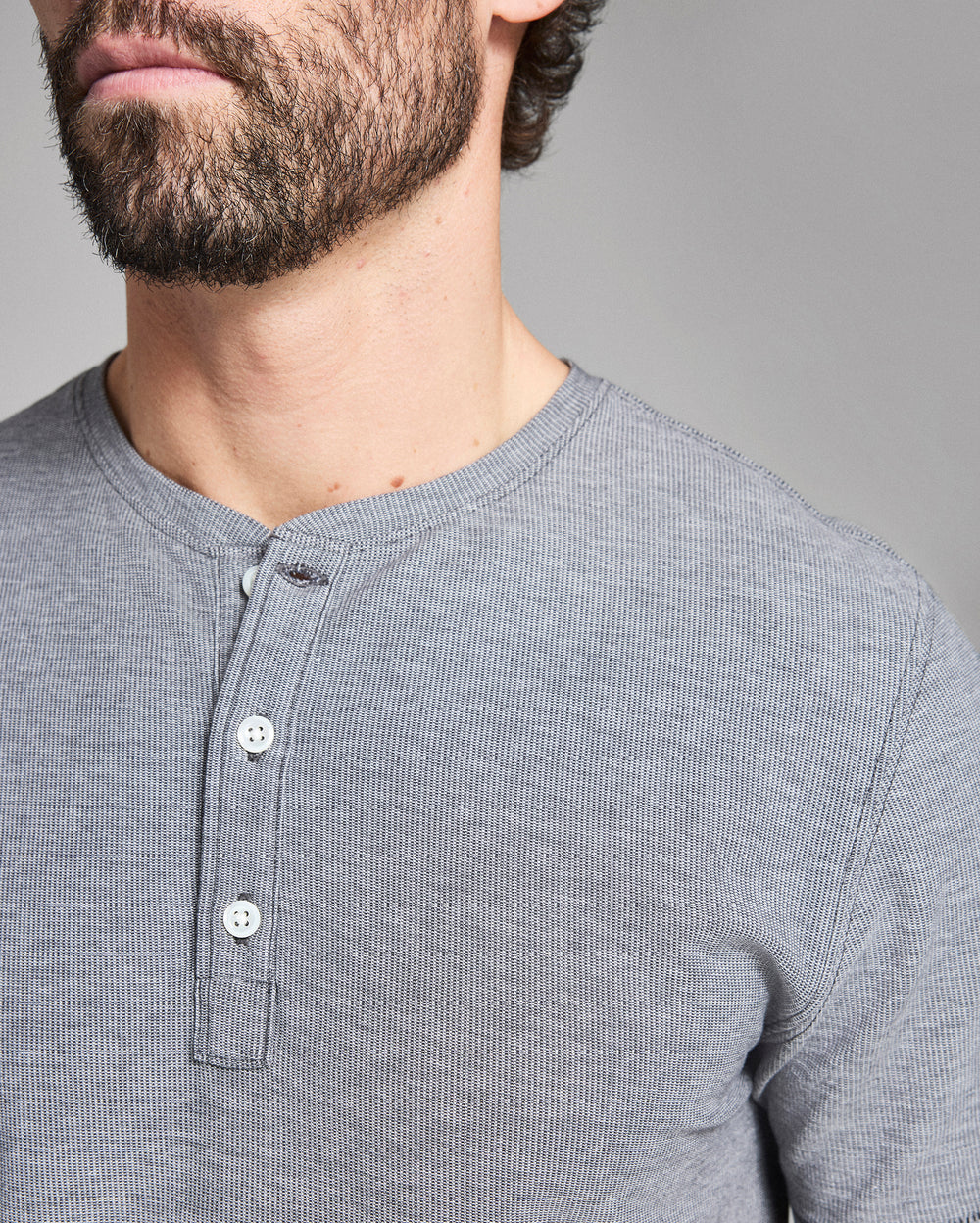 Close-up of a person wearing a gray henley shirt against a gray background
