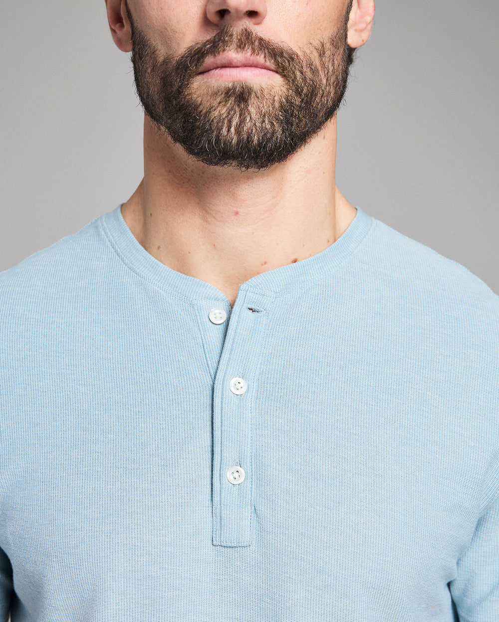 Man wearing a light blue henley shirt against a gray background